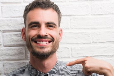 Genç yetişkin adam sürpriz yüz işaret parmağı beyaz tuğla duvarın üzerinden kendisi için ayakta