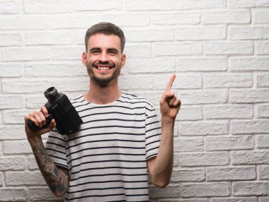Genç adam tutarak kamerayı beyaz tuğla duvar el ve parmak ile tarafına işaret çok mutlu üzerinde duran filme