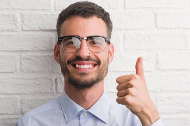 Beyaz tuğla üzerinde duran genç yetişkin iş adamı ok işareti yapıyor büyük gülümseme ile mutlu duvar, parmaklarıyla, mükemmel işaret parmak