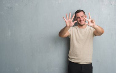 Beyaz delikanlı gösterilen ve parmakları ile işaret gri grunge duvarın üzerinden sekiz kendinden emin ve mutlu gülümseyerek iken numara.