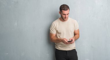 Gri grunge üzerinde beyaz delikanlı duvar manifatura acımak yüz ciddi düşünüyorum üstünde kendine güvenen bir ifade ile smartphone kullanarak bir ileti