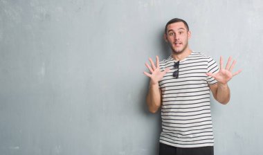 Şokta bağırarak Genç beyaz adam gri grunge duvar korkuyor ve korku ifade dur hareketi el ile ile çok korkmuş. Panik kavramı.