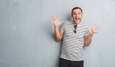 Gri grunge duvar kutluyor üzerinde beyaz delikanlı deli ve çığlık kaldırdı ve açık gözleri heyecanlı silah ile başarı için hayran. Kazanan kavramı