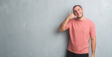 Üzerinde gri grunge duvar gülümseyen Genç beyaz adam el ve parmak telefonda konuşmak ile telefon jest yapıyor. Kavramları iletişim.