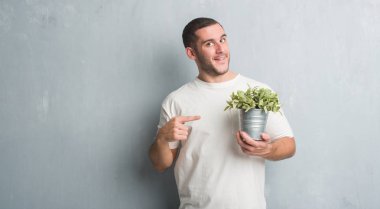 Bitki pot çok mutlu el ve parmak ile işaret tutan gri grunge duvarın üzerinden beyaz delikanlı