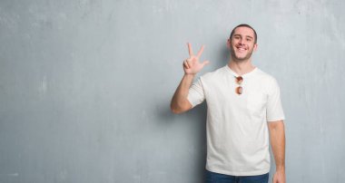 Beyaz delikanlı gösterilen ve parmakları ile işaret güneş gözlüğü takıyor gri grunge duvarın üzerinden üçüncü ise kendinden emin ve mutlu gülümseyerek.