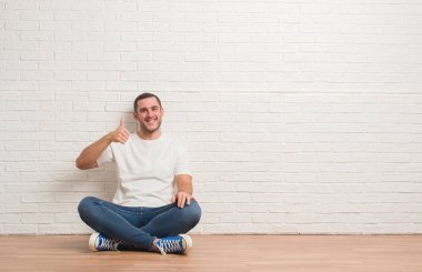 Hareketi el ile mutlu yaşasın yapıyor beyaz tuğla duvarın üzerinden katta oturan beyaz delikanlı. Kameraya bakarak başarı gösteren ile ifade onaylama.