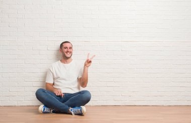 Mutlu yüz zafer işareti yaparken kameraya göz kırpıyor ile gülümseyen beyaz tuğla duvarın üzerinden katta oturan beyaz delikanlı. İki numaralı.