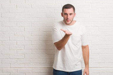 Bir öpücük el ile güzel ve seksi olmak hava üfleme kamera bakıyor beyaz tuğla duvarın üzerinden ayakta beyaz delikanlı. Aşk ifade.