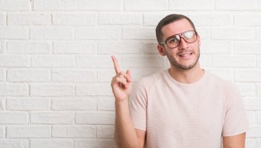 El ve parmak ile tarafına işaret çok mutlu gözlüklü beyaz tuğla duvarın üzerinden ayakta beyaz delikanlı