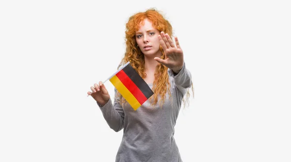 防衛ジェスチャー 深刻な自信を持って式に一時停止の標識をやって開いた手とドイツの国旗を保持している赤毛の若い女性 — ストック写真