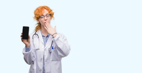 Unga Rödhårig Läkare Kvinna Visar Smartphone Täcker Munnen Med Handen — Stockfoto