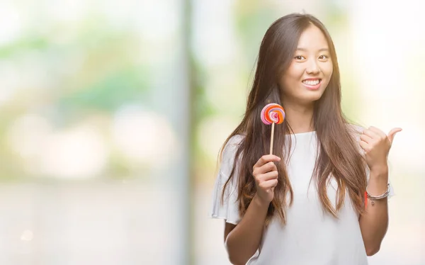 Joven Mujer Asiática Comiendo Caramelos Piruleta Sobre Fondo Aislado Señalando —  Fotos de Stock
