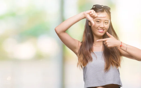 若いアジアの女性は 笑顔と幸せそうな顔で指手作りフレーム分離の背景の上にサングラスをかけています 創造性と写真のコンセプト — ストック写真