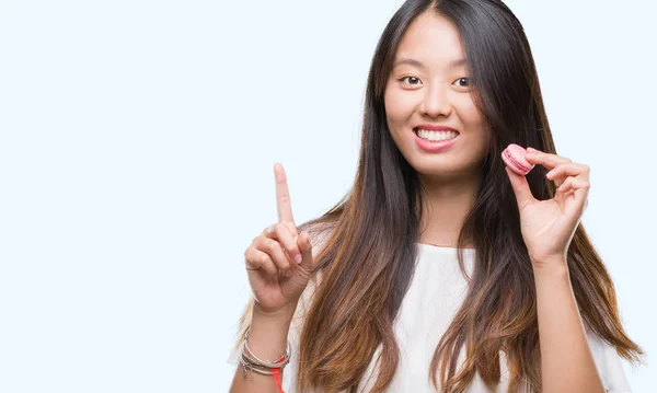 考えや疑問 ナンバーワンの幸せそうな顔で指を指していると驚かれる分離の背景にピンクのマカロンの甘いを食べる若いアジア女性 — ストック写真