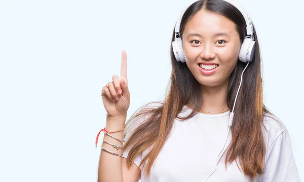 幸せそうな顔 ナンバーワンのアイデアや質問ポインティング指で身に着けているヘッドフォンの分離された背景音楽を聴く若いアジア女性を驚かせた — ストック写真