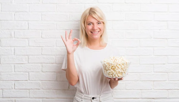 優秀なシンボルの指で サインをしてポップコーンを食べる白いレンガ壁を越えて大人の白人女性 — ストック写真