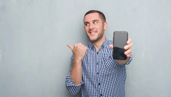 Joven Hombre Caucásico Sobre Pared Grunge Gris Mostrando Pantalla Blanco — Foto de Stock