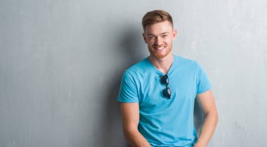 Gri grunge duvar yüzündeki mutlu ve güzel bir gülümseme ile gündelik kıyafeti giymiş genç Kızıl saçlı adam. Şanslı kişi.