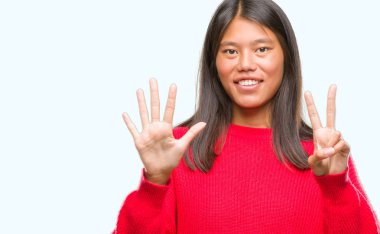 Genç Asyalı kadın giyiyor kış kazak gösterilen ve parmakları ile işaret izole arka plan üzerinde kendinden emin ve mutlu gülümseyerek süre yedi numara.