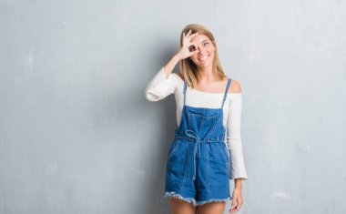 Gülümseyen, parmakları ile mutlu yüz üzerinden seyir göz el ile ok jest yapıyor grunge gri duvar üzerinde duran güzel genç kadın.