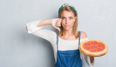 Kızgın yüz, eksi işareti aşağı antipati başparmak ile gösterilen, ret kavramı ile biberli pizza yeme grunge gri duvar güzel genç kadın