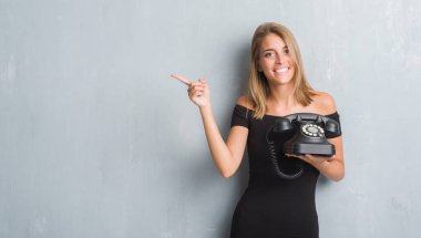 Güzel genç kadın vintage telefon çok mutlu el ve parmak ile tarafına işaret tutan grunge gri duvarın üzerinden