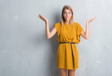 Bir elbise clueless ve şaşkın ifadeyle kollar ve eller kaldırdı giyen grunge gri duvar üzerinde duran güzel genç kadın. Şüphe kavramı.