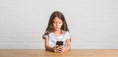 Acımak yüz ciddi düşünüyorum üstünde kendine güvenen bir ifade ile smartphone kullanarak masada oturan genç İspanyol çocuk