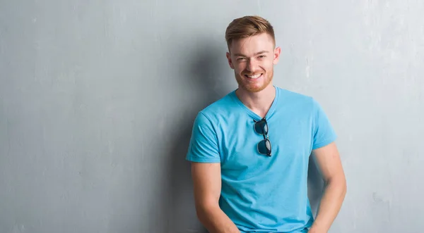 Young redhead man over grey grunge wall wearing casual outfit with a happy and cool smile on face. Lucky person.