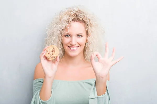 Joven Mujer Rubia Sobre Grunge Gris Pared Comer Chocolate Chip —  Fotos de Stock