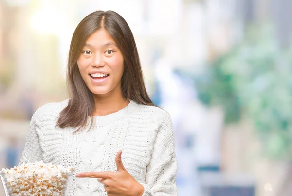 Молодая Азиатская Женщина Ест Попкорн Изолированном Фоне Счастливо Указывая Рукой — стоковое фото