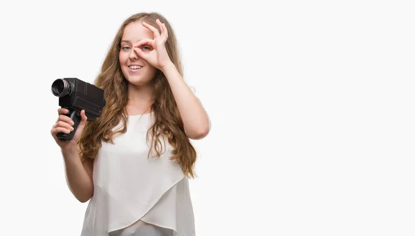 年轻的金发女子手持超级8视频相机与快乐的脸微笑做 标志与手在眼睛看通过手指 — 图库照片