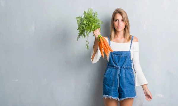 Vacker Ung Kvinna Över Grunge Grå Väggen Håller Färska Morötter — Stockfoto