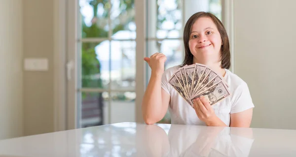 唐氏综合症妇女在家里拿着美元指着和显示与拇指向上微笑的一面与快乐的脸 — 图库照片