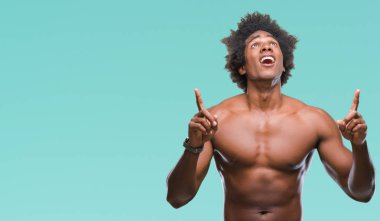 Afro Amerikalı gömleksiz adam çıplak vücut izole arka plan üzerinde gösterilen hayrete ve yukarıya bakıyor ve parmakları ile işaret ve silah kaldırdı şaşırttı.