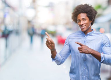 Gülümseyen ve iki elleri ve parmakları ile tarafına işaret kamera bakarak izole arka plan üzerinde Afro Amerikalı adam.