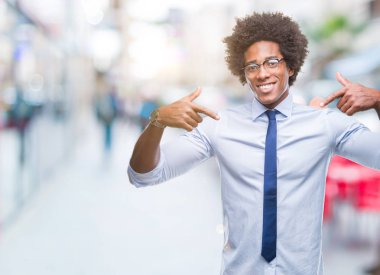 Yüzünde gülümseme ile kendinden emin görünüyorsun, kendini gururlu ve mutlu parmakları ile işaret izole arka plan üzerinde gözlük takan Afro Amerikalı iş adamı.