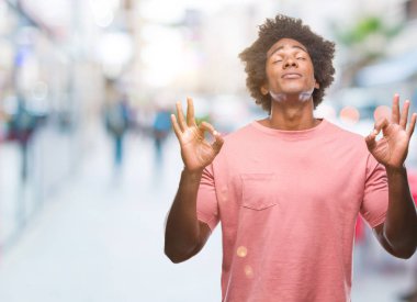 İzole arka plan üzerinde Afro Amerikalı adam rahatla ve gülümseyen gözlerle kapalı parmak jestle meditasyon yapıyor. Yoga kavramı.