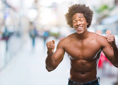 Afro Amerikalı gömleksiz adam çıplak vücut izole arka plan üzerinde silah ile başarı için heyecanlı gösterilen zafer kutluyor gülümseyen kaldırdı. Kazanan kavramı.