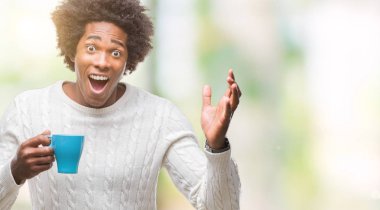 Kocaman bir gülümseme ile çığlık zaferini kutluyor ve ellerini kaldırdı izole arka plan çok mutlu ve heyecanlı, kazanan ifade üzerinde kahve içme Afro Amerikalı adam