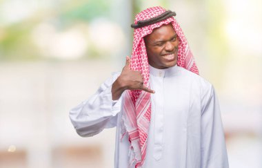 Geleneksel keffiyeh yapıyor gülümseyen izole arka plan üzerinde giyen genç Arapça Afrika adam telefon hareketi ile el ve parmak telefonda konuşuyor gibi. Kavramları iletişim.