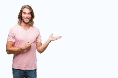 Hayret ve el ile sunulması ve parmak ile işaret ederken kameraya gülümseyen izole arka plan üzerinde uzun saçlı yakışıklı delikanlı.