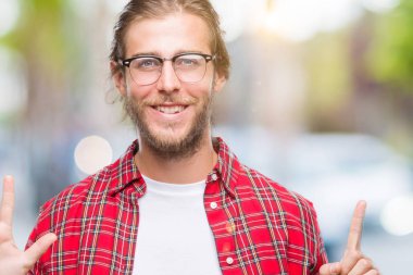 Genç yakışıklı adam uzun saçlı gözlük üzerinde gösterilen ve parmakları ile işaret izole arka plan ile kendinden emin ve mutlu gülümseyerek süre 6 numara.