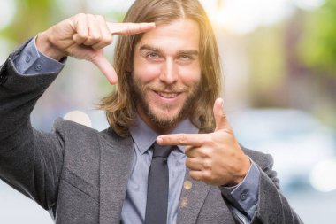 Elle yapma çerçeve ve parmakları ile mutlu yüz gülümseyen izole arka plan üzerinde uzun saçlı Genç yakışıklı iş adamı. Yaratıcılık ve Fotoğrafçılık kavramı.