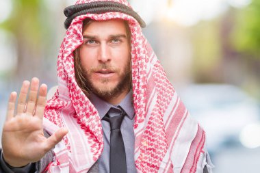 Genç yakışıklı Arap adam uzun saçlı keffiyeh stop yapıyor izole arka plan üzerinde giyen elin avuç ile şarkı. Negatif ve ciddi bir jest yüz ifadesiyle uyarı.