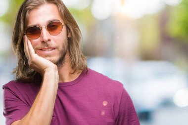 Seyir yorgun ve bıkkın ile depresyon sorun Çapraz kollar ile izole arka plan düşünme üzerinde güneş gözlüğü takmış uzun saçlı yakışıklı delikanlı.