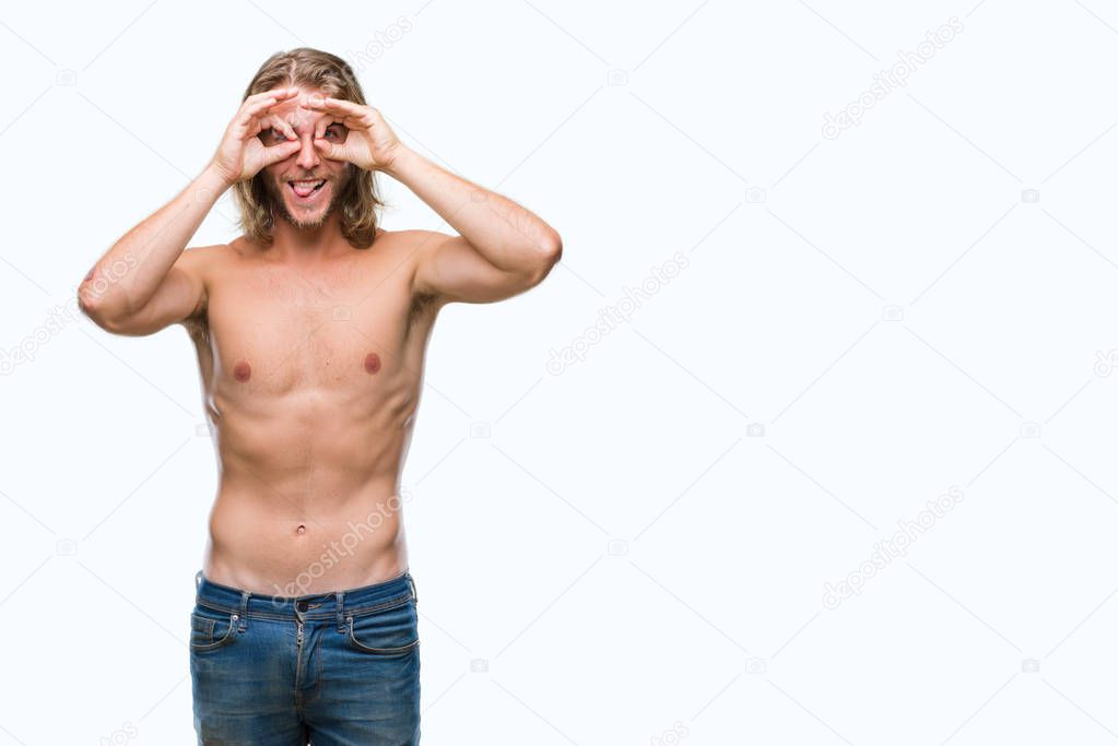 Young handsome shirtless man with long hair showing sexy body over isolated background doing ok gesture like binoculars sticking tongue out, eyes looking through fingers. Crazy expression.