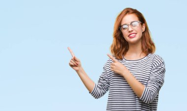 İzole arka plan gülümseyen ve iki elleri ve parmakları ile tarafına işaret kamera bakarak gözlüklü genç güzel kadın.