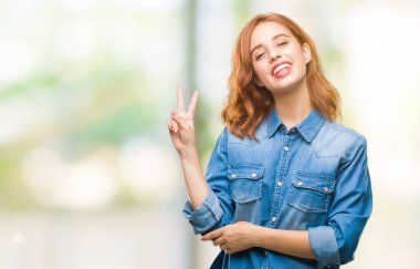 Genç güzel kadın mutlu yüz zafer işareti yaparken kameraya göz kırpıyor ile gülümseyen izole arka plan yüzünden. İki numaralı.